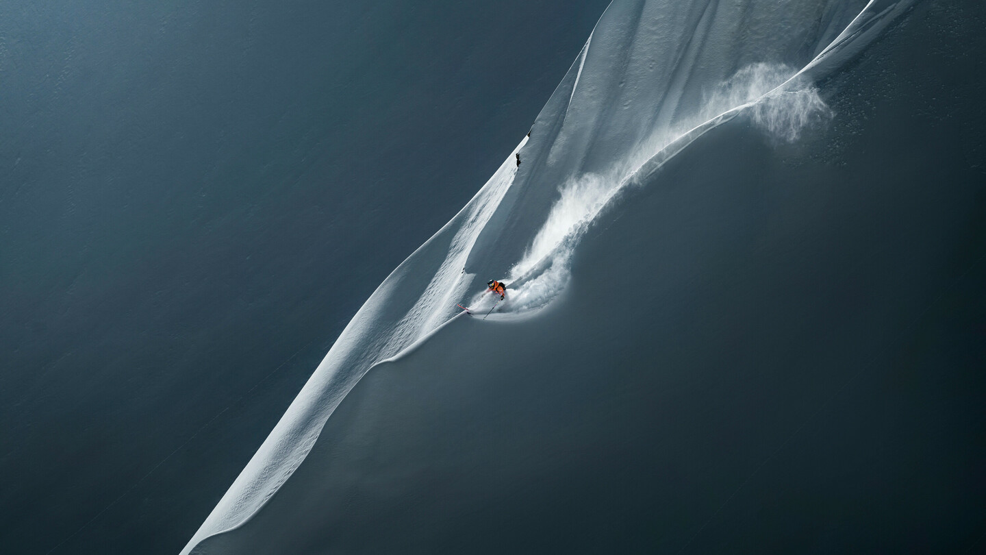 Skifahrer fährt eine steile, unberührte Schneefläche hinunter und hinterlässt eine dynamische Spur im frischen Pulverschnee.